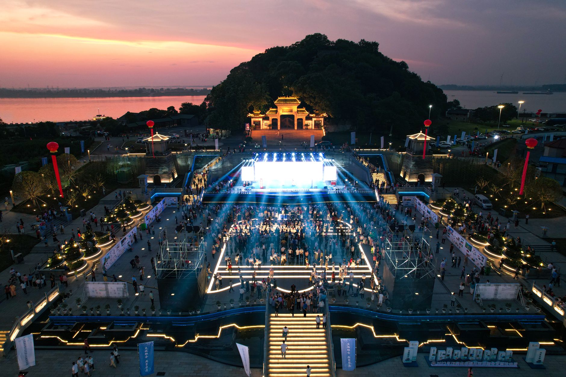 An outdoor concert stage lit up in a riverside park at night