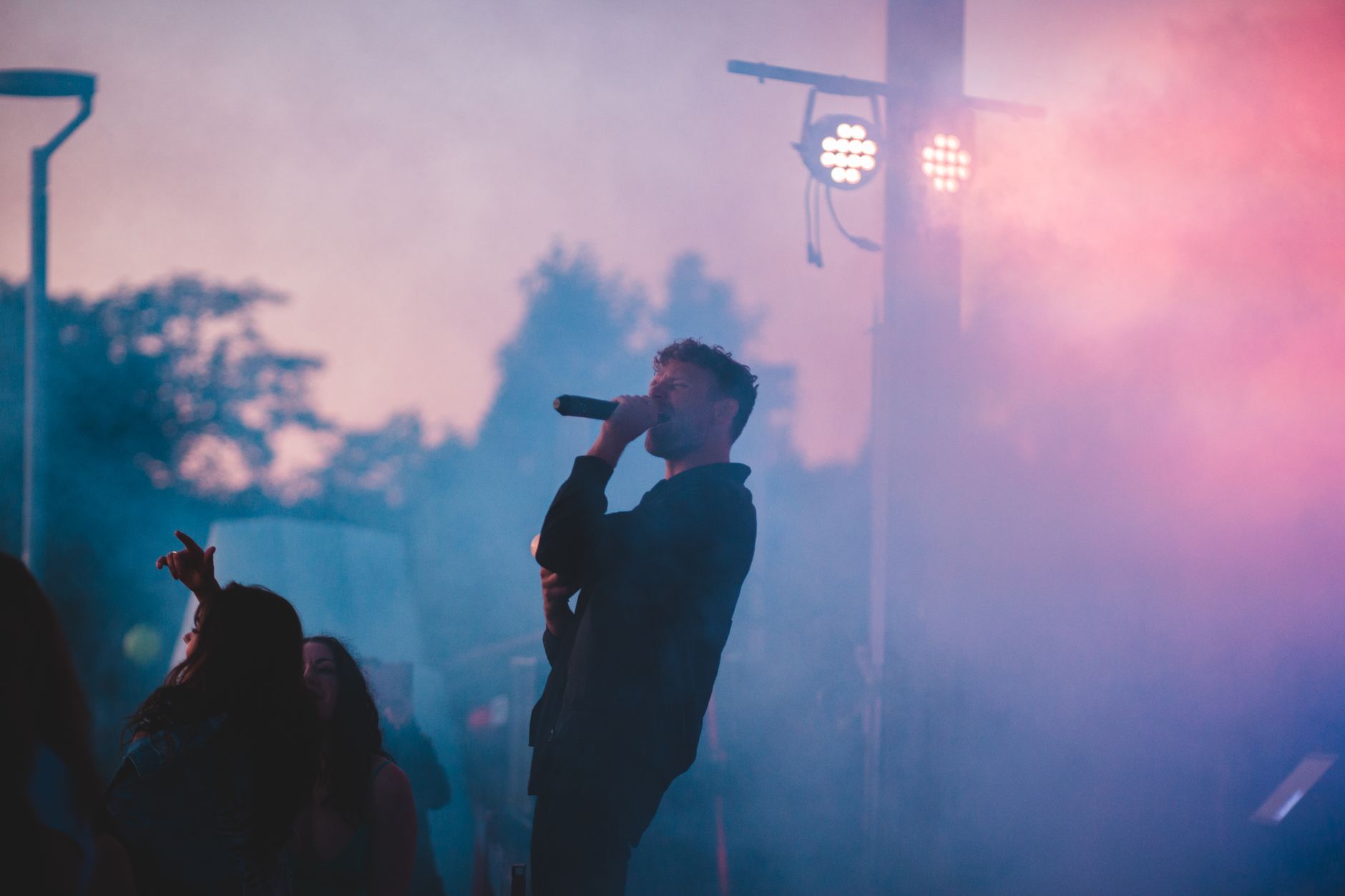 A singer performing on the outdoor festival stage at dusk, bathed in stage lights